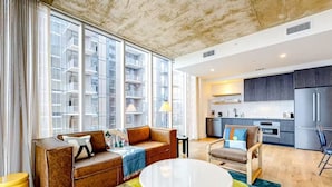 A modern living room with a brown leather sofa, a round white coffee table, and a view of a cityscape through large windows.