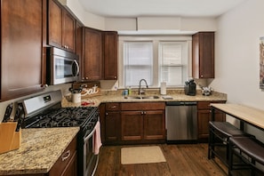 A kitchen with dark wooden cabinets, a granite countertop, stainless steel appliances, and a built-in dishwasher.