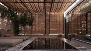 Un moderno espacio de spa con suelo calefaccionado, un sofá y un ventanal con persianas de bambú.