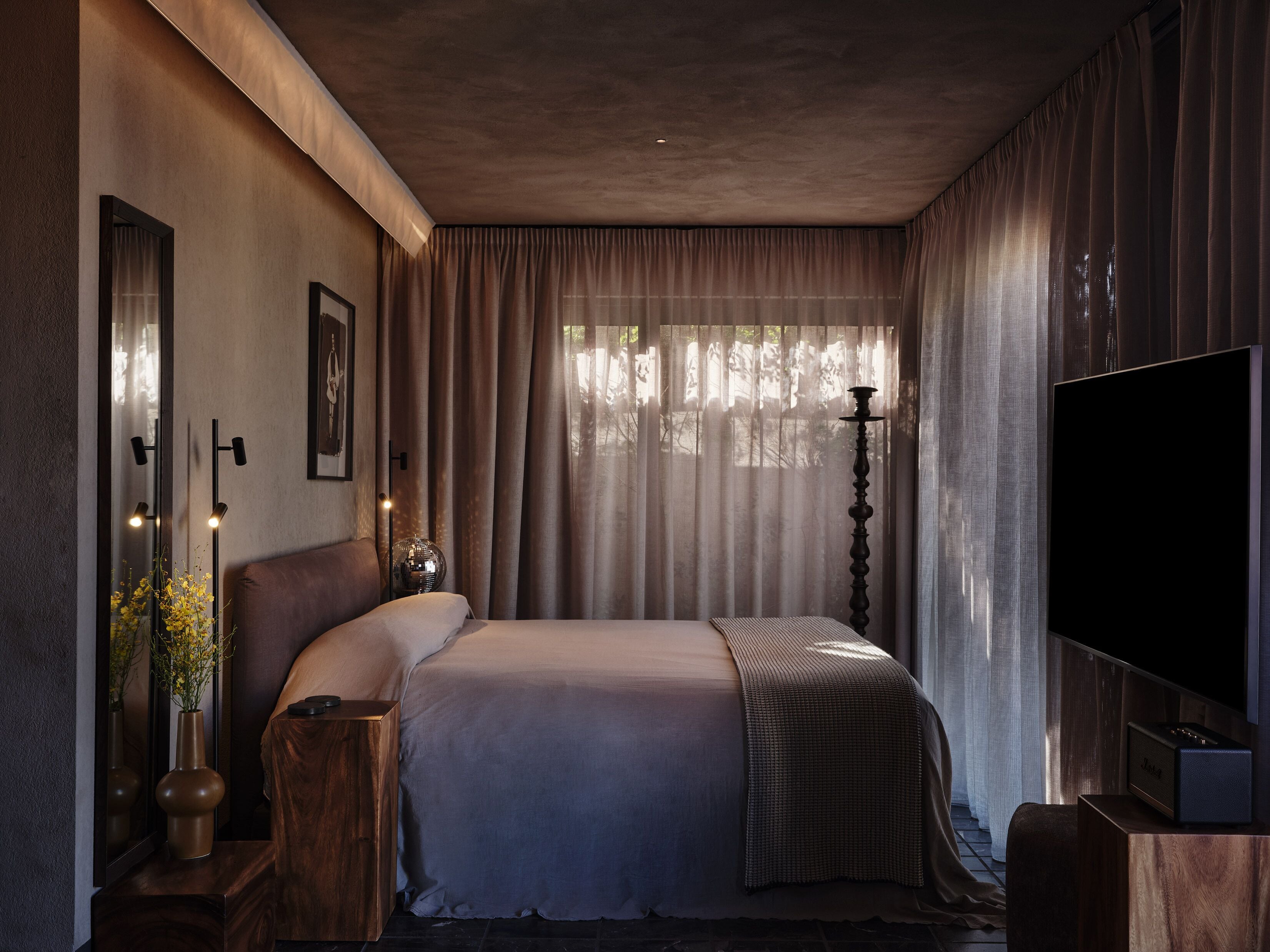 Une chambre à coucher avec un grand lit, un téléviseur à écran plat, une table de chevet avec une lampe et une fenêtre avec des rideaux.