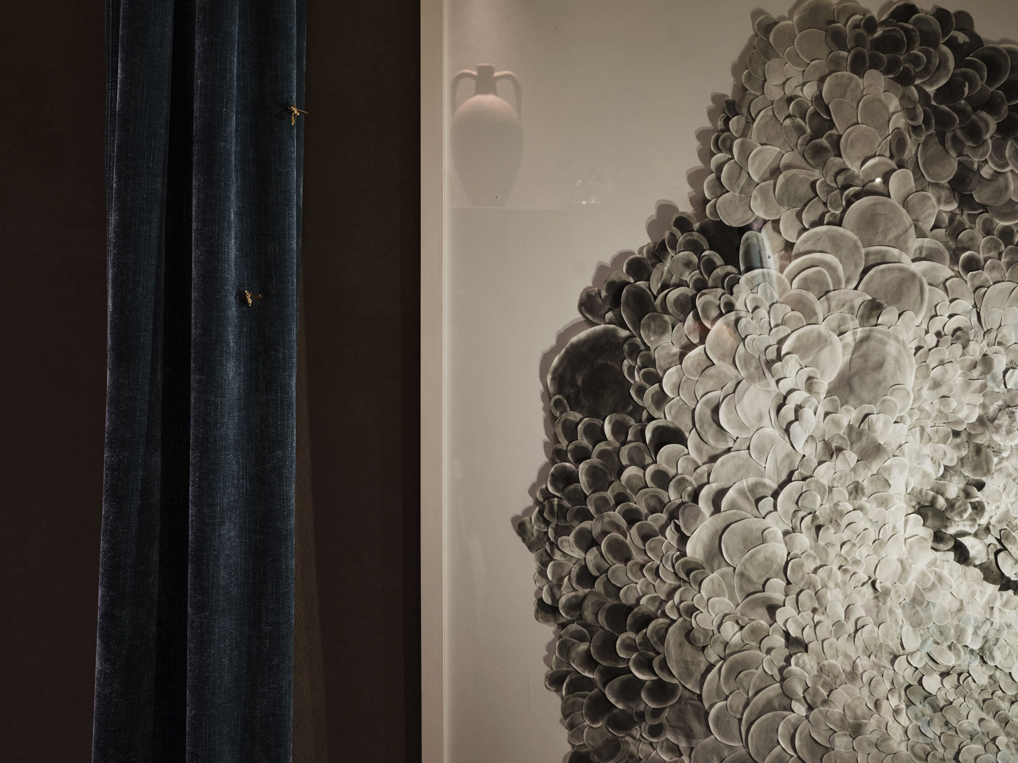 A room with a large, textured wall art piece and a dark curtain.
