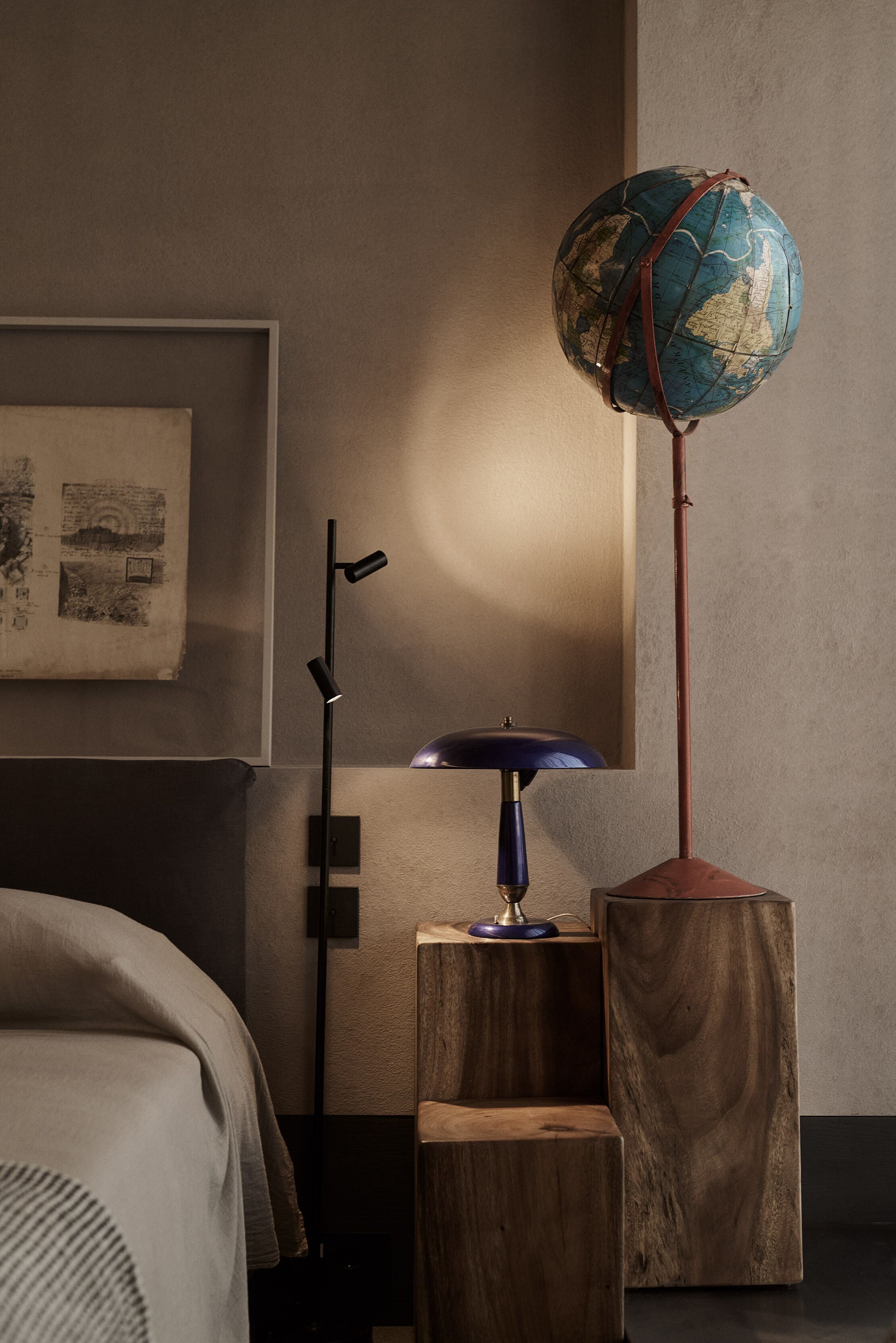 A modern bedroom with a globe lamp, wooden nightstands, and a framed map on the wall.