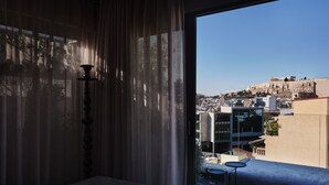 Habitación de hotel con un gran ventanal que da a un paisaje urbano y ruinas antiguas.