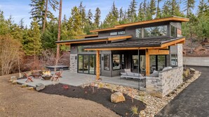 Ein modernes, zweistöckiges Haus mit Natursteinfassade, großen Glasfenstern und einer Terrasse mit Sitzgelegenheit.