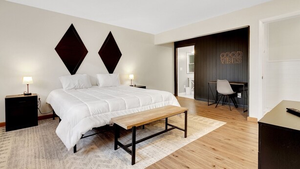 A modern bedroom with a large bed, bedside tables, a bench, a desk, and a chair. - House on The Rocks with EV Charger (Chittenden)