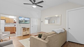 A modern living room with a sofa, a coffee table, a TV, and a ceiling fan. - Apt W/ heated garage Libertyville Near Naval Base (Libertyville)