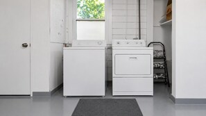 A laundry room with a washing machine and dryer, a window with blinds, and a metal shelf unit.