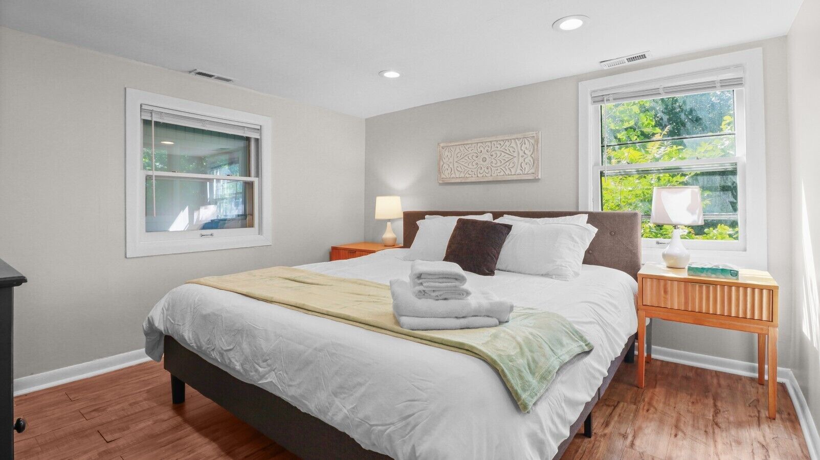 A bedroom with a bed, bedside tables, a window, and a wall-mounted artwork.