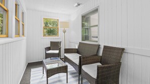 A room with white paneled walls, a wicker sofa, a matching chair, a glass coffee table, and a floor lamp.