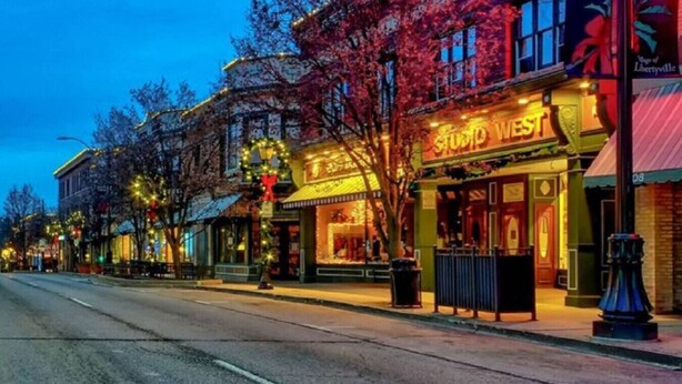 A street view of a commercial area with storefronts, including a brightly lit building with a sign that reads "STUDIO WEST". - Apt W/ heated garage Libertyville Near Naval Base (Libertyville)