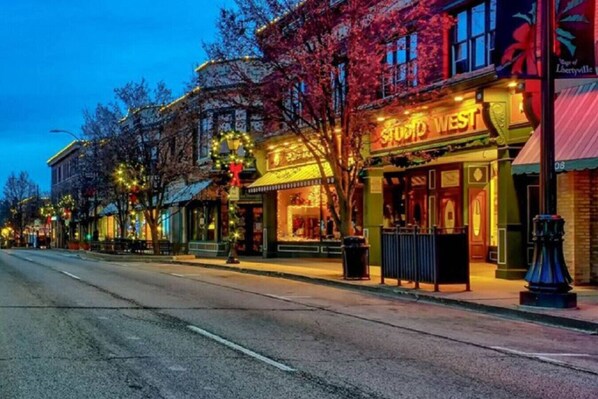 A street view of a commercial area with storefronts, including a brightly lit building with a sign that reads "STUDIO WEST". - Apt W/ heated garage Libertyville Near Naval Base (Libertyville)