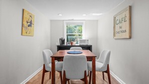 A dining area with a wooden table and four chairs, a window with a view of greenery, a coffee maker, and a microwave on a black countertop.