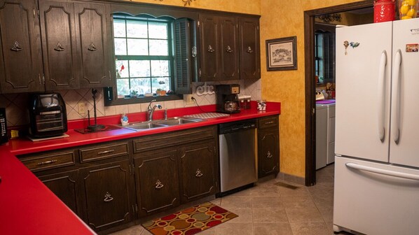 A kitchen with dark wooden cabinets, a red countertop, a stainless steel dishwasher, and a white refrigerator.
