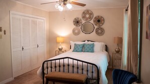 Un dormitorio con cama, mesitas de noche, un banco, ventilador de techo y decoración mural.
