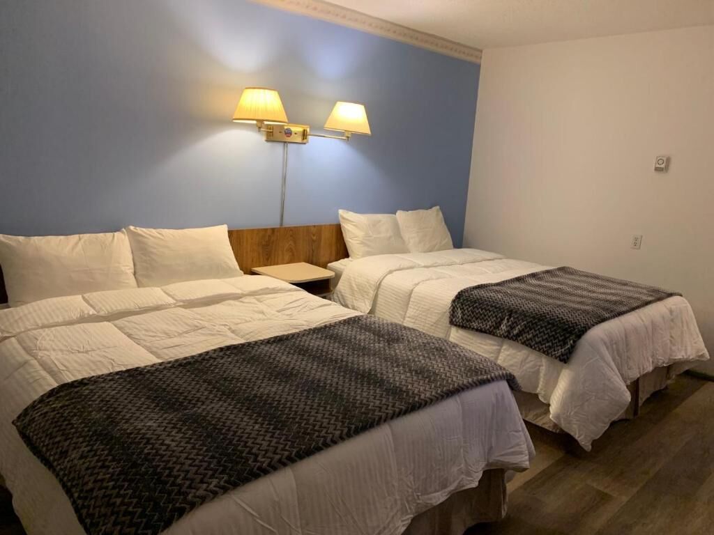 A hotel room with two beds, a wooden headboard, and two wall-mounted lamps.
