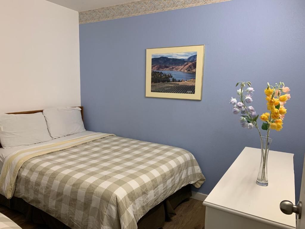 Un dormitorio con cama, una mesita de noche con un florero y un cuadro en la pared.