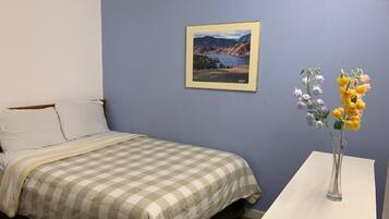 Un dormitorio con cama, una mesita de noche con un florero y un cuadro en la pared.