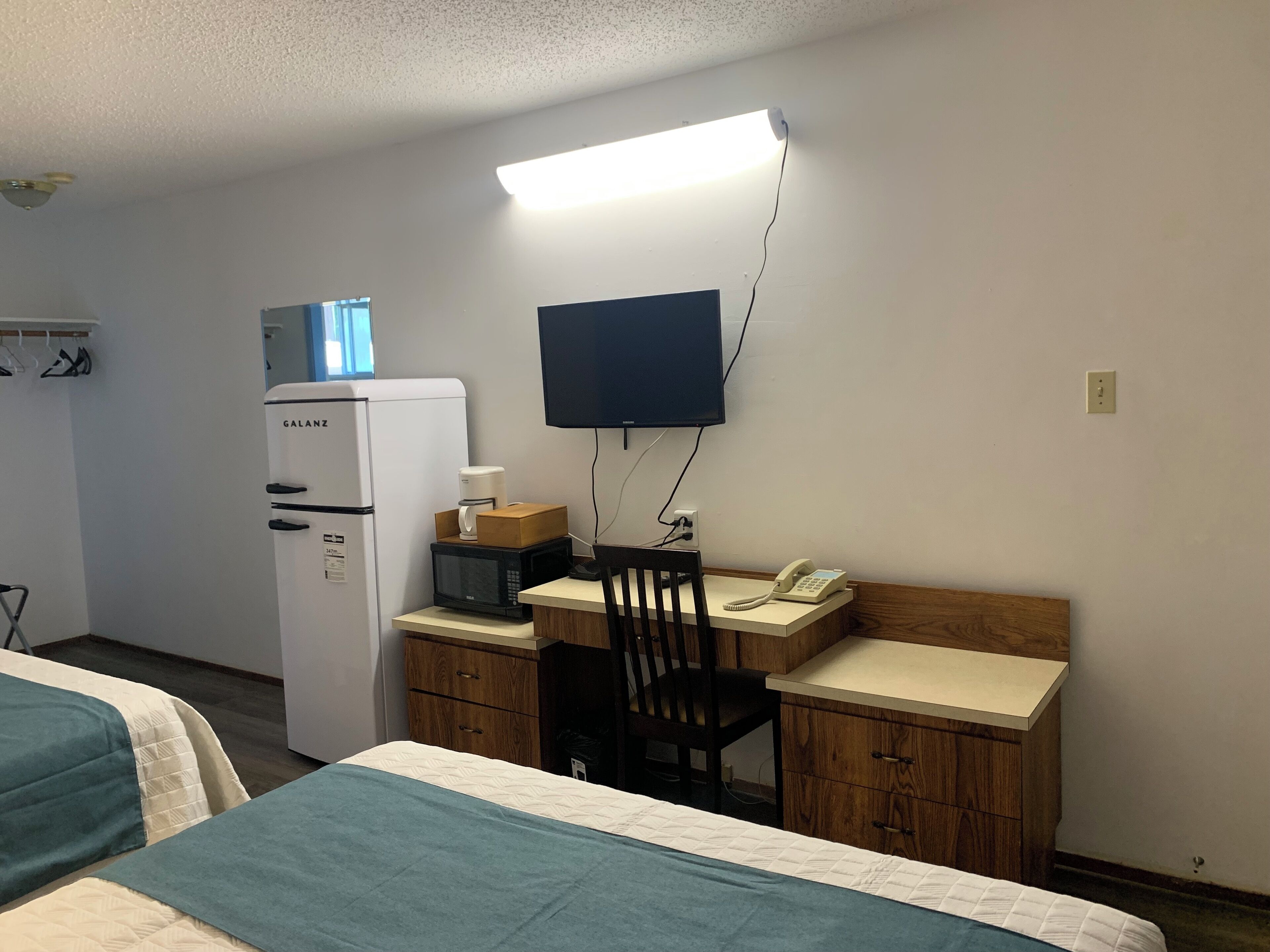 Ein Hotelzimmer mit einem Bett, einem Schreibtisch mit Stuhl, einer Mikrowelle, einem Kühlschrank, einem Fernseher und einem Telefon.