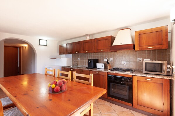 Una cocina con armarios de madera, encimera de granito, estufa, microondas y una mesa de comedor con fruta.