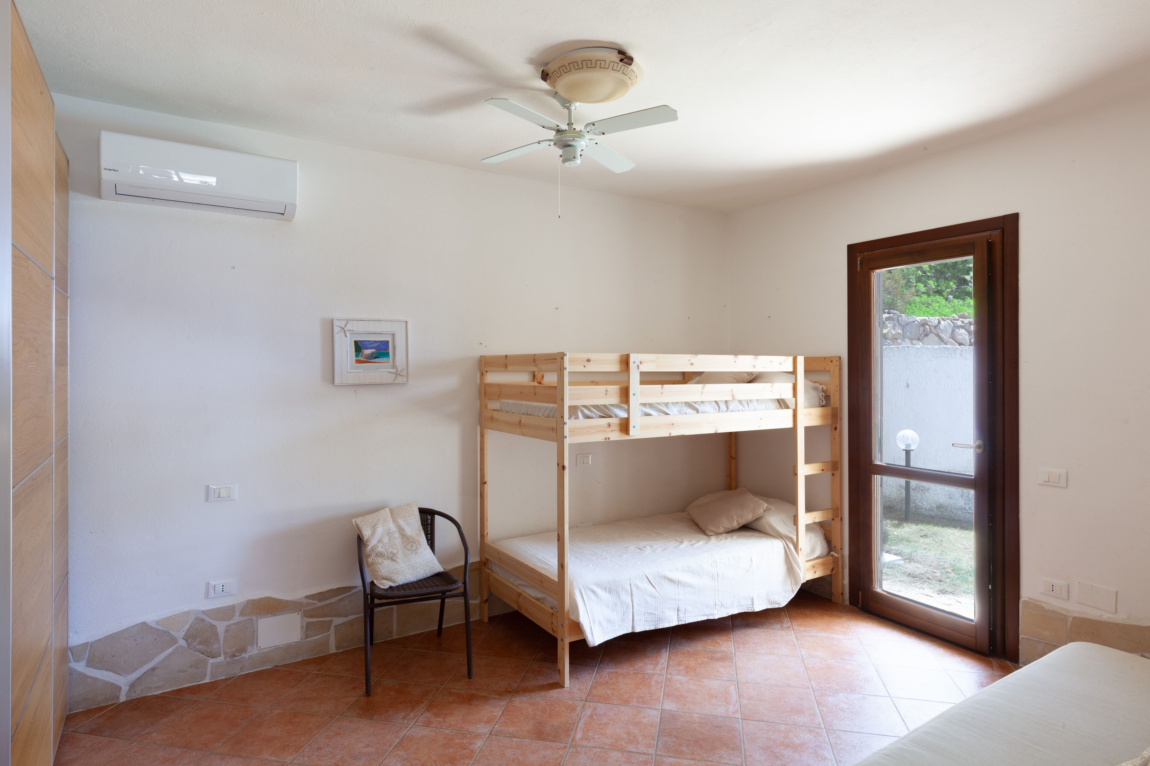 A room with a bunk bed, a ceiling fan, a window, and a chair.