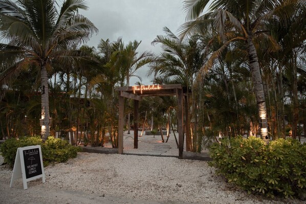 A tropical resort entrance with a wooden archway labeled "The Pool Club" and a sign indicating breakfast, lunch, and dinner services. - Tranquility & Mistico Beach Club + Boat Shuttle (San Pedro)
