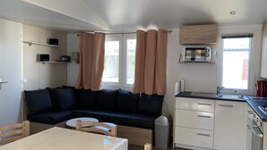 Ein kompakter Wohnbereich mit Sofa, Esstisch, Küchenzeile und einem Fenster mit Vorhängen.
