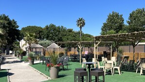 Ein Außenbereich mit einer Holz-Pergola, verschiedenen Sitzgelegenheiten und grünem Kunstrasen.