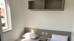 Ein kompaktes Hotelzimmer mit zwei Einzelbetten, einem kleinen Nachttisch und einem fest installierten Regal über den Betten.