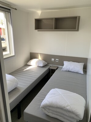 Two single beds with white bedding and pillows, a bedside table, and storage shelf.