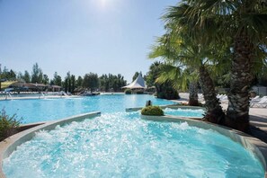 Relax by the serene pool surrounded by palm trees and lounge chairs, featuring a soothing waterfall.