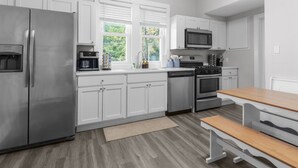 A modern kitchen with white cabinets, stainless steel appliances, a built-in oven, and a window with a view of greenery. - Cozy W Front Porch DT Libertyville near Naval Base (Libertyville)