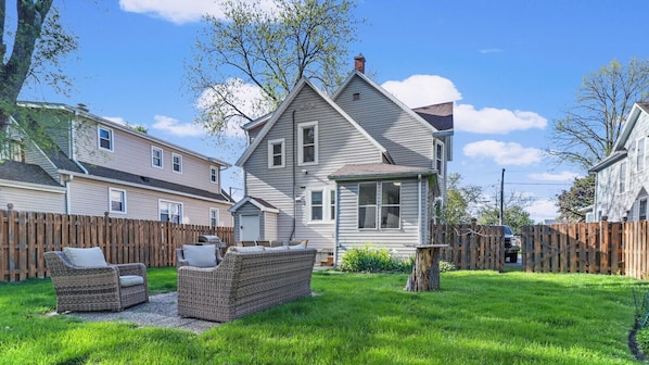 A residential property with a two-story house, a fenced backyard, and outdoor furniture.