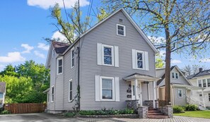 A two-story house with a front porch, a brick driveway, and a wooden fence.