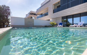 Ett modernt poolområde med kristallklart vatten, solstolar och en modern byggnad med balkonger.