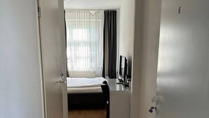 A hotel room with a bed, a desk, a chair, a window with curtains, and a door. - Upper-House (Aystetten)