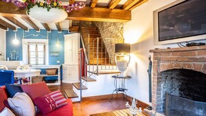 Un salon chaleureux avec une cheminée, un escalier et un coin repas aux murs bleus et aux poutres en bois.