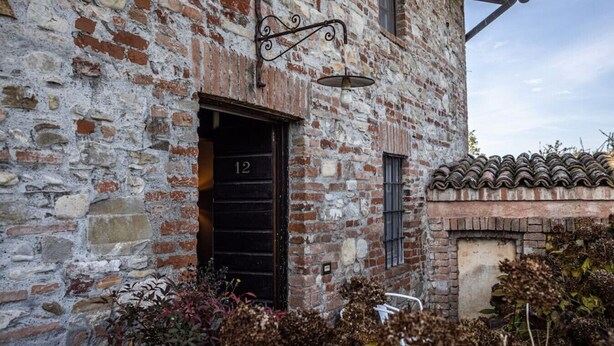 Un bâtiment rustique en pierre, doté d’une porte noire portant le numéro « 12 », d’une petite fenêtre et d’un toit traditionnel recouvert de tuiles.