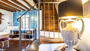 Un escalier avec une rampe en métal menant à un plancher en bois, une lampe blanche avec un abat-jour noir et un mur bleu orné d’un motif représentant un oiseau.