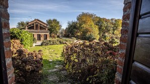 Une maison de campagne à l’aspect rustique, avec une façade en briques, un chemin de pierre menant à la porte d’entrée et un jardin agrémenté de diverses plantes et arbres.