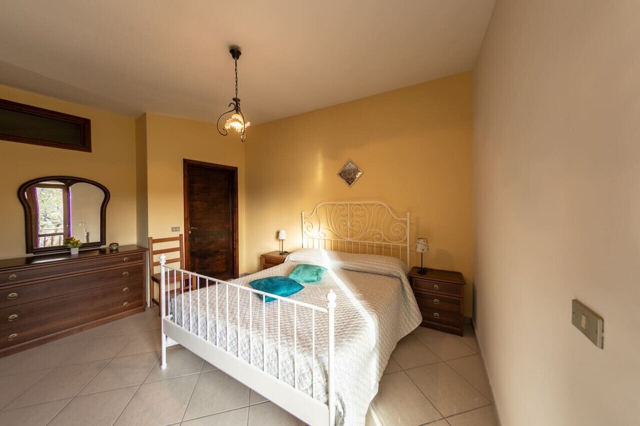 Une chambre à coucher avec un lit en métal blanc, une commode en bois, une table de chevet avec une lampe et un luminaire suspendu.