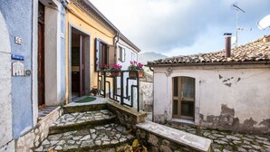 A narrow street with cobblestone steps leading to a building with a white facade and a balcony with potted plants. - La Casetta dei Gerani (Montemarano)