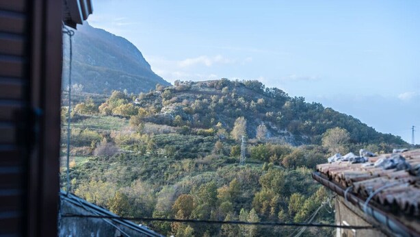 A view of a mountainous landscape with a power line tower and a building with a tiled roof. - La Casetta dei Gerani (Montemarano)