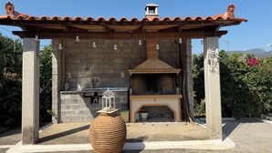 An outdoor kitchen with a brick chimney, hanging lights, and a large ceramic pot. - Andrea's House 
 (Valira)