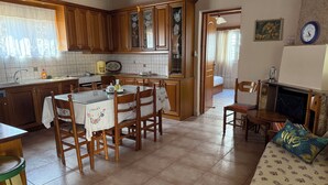 A kitchen with wooden cabinets, a dining table with chairs, a tiled floor, and a fireplace. - Andrea's House 
 (Valira)