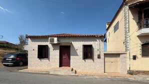 A two-story building with a red door, a small porch, and a car parked in front. - Andrea's House 
 (Valira)