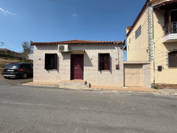 A two-story building with a red door, a small porch, and a car parked in front. - Andrea's House
(Valira)