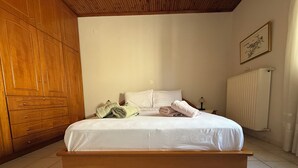 A bedroom with a wooden bed frame, white bedding, and a radiator on the wall. - Andrea's House 
 (Valira)