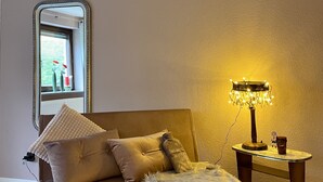 A cozy room with a sofa, a small table with a lamp, and a window with flowers.