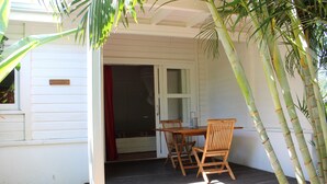 A wooden table and chairs on a porch with a white exterior wall and a sliding glass door.