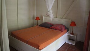 A single bed with an orange bedspread, two pillows, a white headboard, and two bedside tables with red lamps.